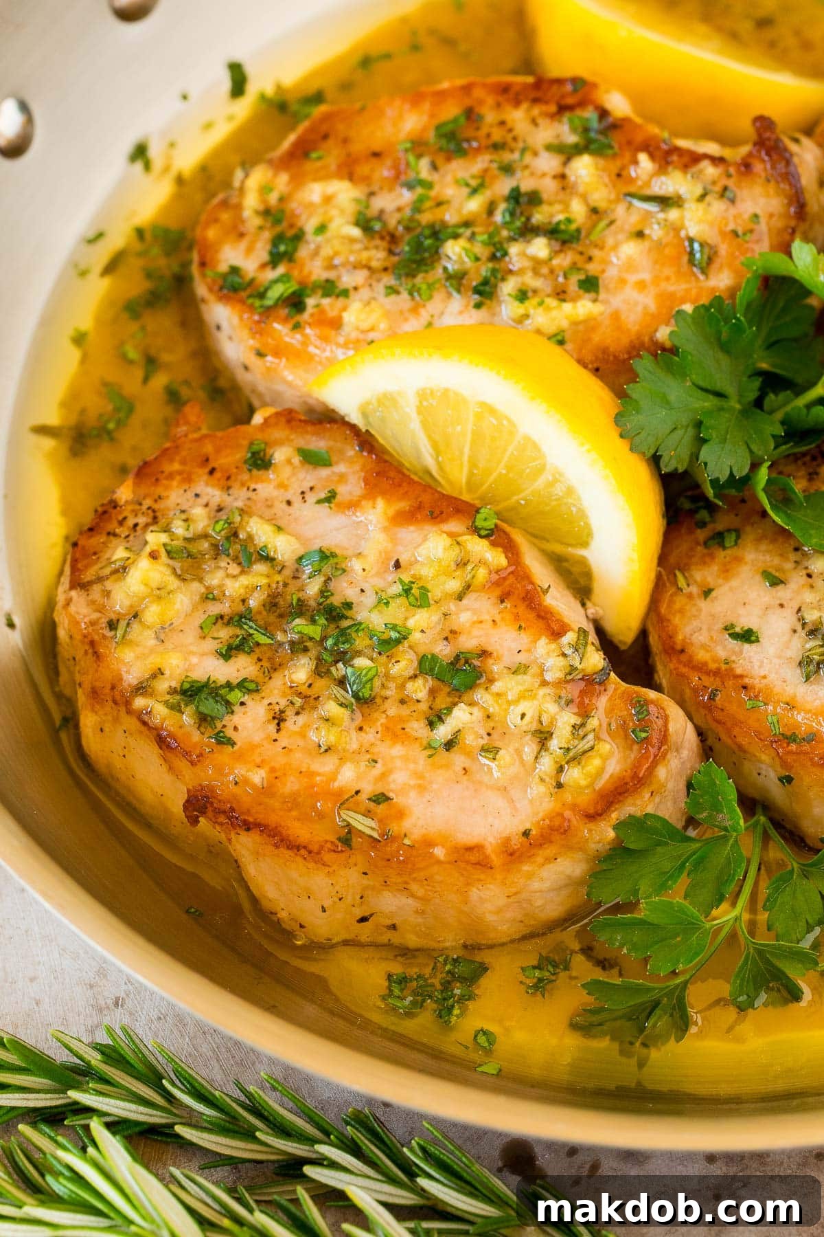 Oven-baked boneless pork chops presented in a pan, garnished with fresh lemon slices and parsley for a bright, appetizing display.
