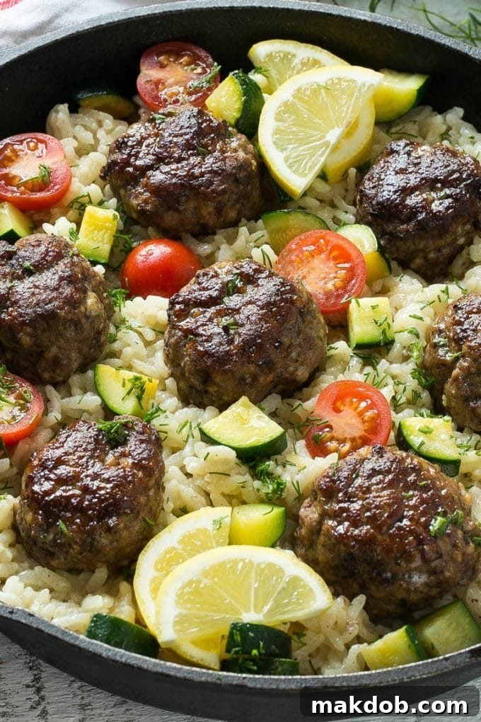 Baked Greek meatballs in a skillet with creamy rice, vibrant cherry tomatoes, and tender zucchini.
