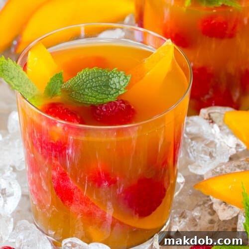 A glass of mango iced tea garnished with fresh fruit and mint.