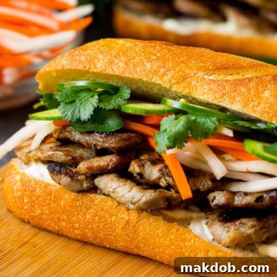 A beautifully layered Banh Mi sandwich ready to be served, showcasing the grilled pork, vibrant pickled vegetables, and fresh herbs in a crusty French roll.