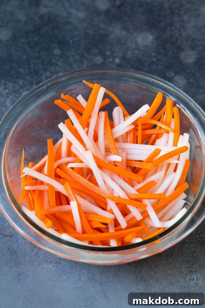 A bowl filled with finely shredded carrots and daikon radish, vibrant and ready for pickling, showcasing the fresh ingredients for Banh Mi.
