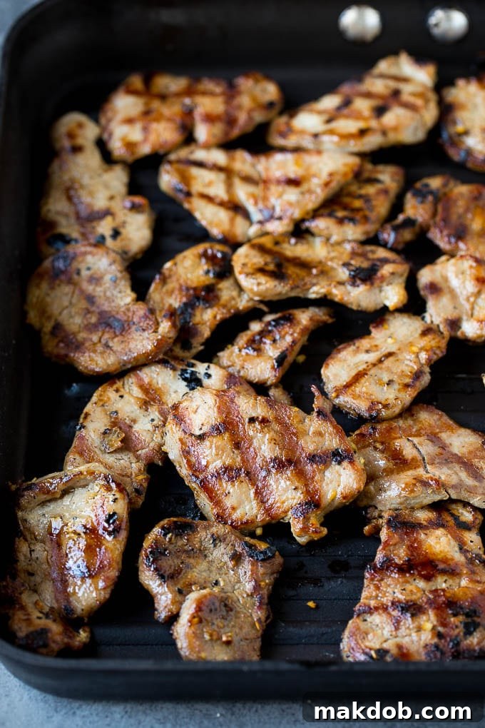 Thinly sliced, marinated pork tenderloin sizzling on a hot grill pan, getting perfectly browned and caramelized for the Banh Mi.