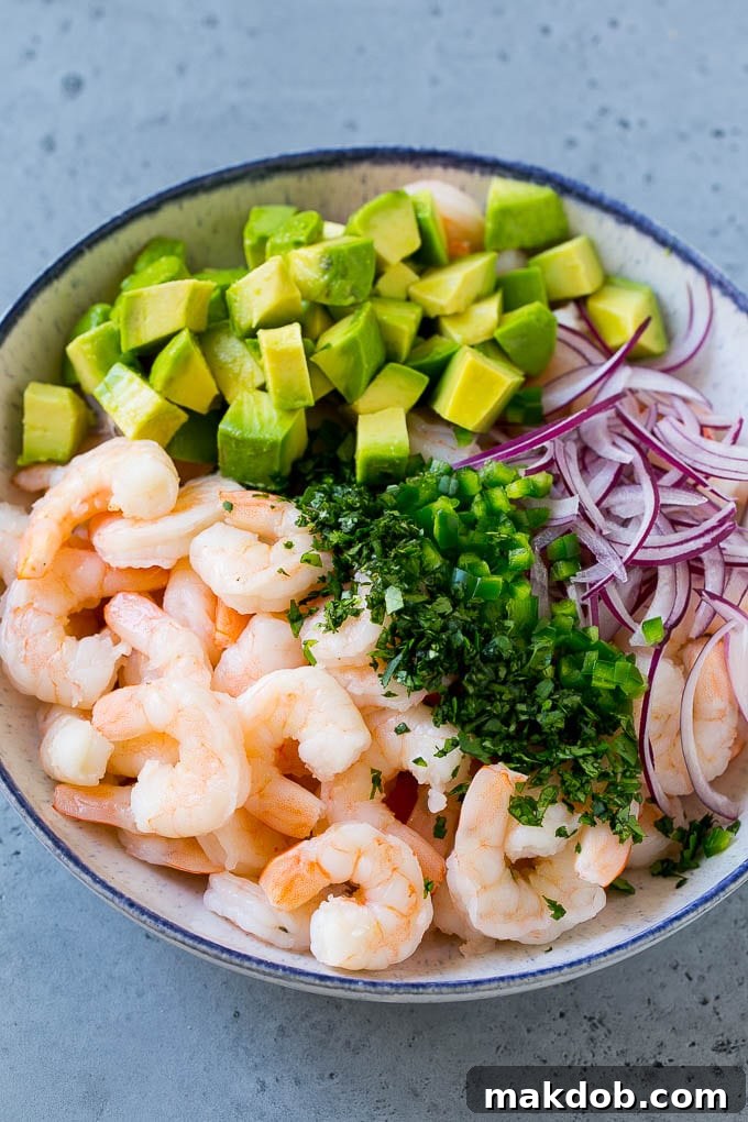 Close-up shot of a serving bowl filled with a colorful mix of shrimp, thinly sliced red onion, creamy avocado cubes, fresh green jalapeno, and vibrant cilantro, ready to be combined with the cocktail sauce.