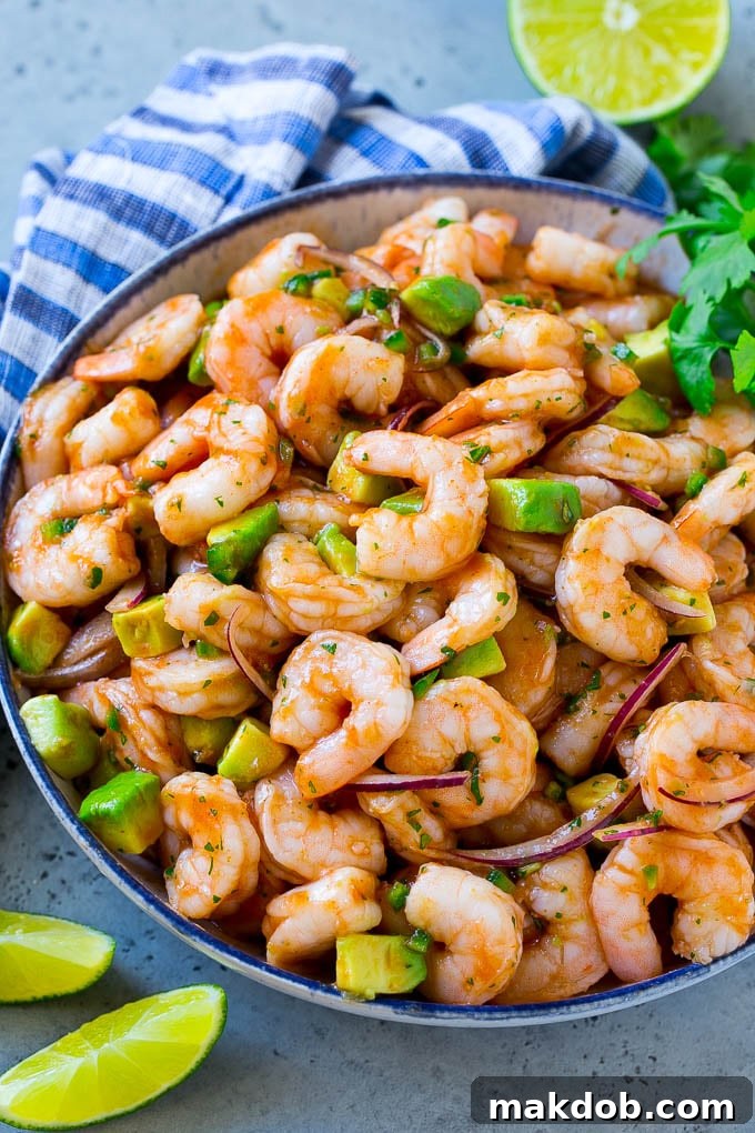 A large, vibrant bowl of Mexican shrimp cocktail, featuring an abundance of cooked shrimp, fresh red onion, creamy avocado, and green cilantro, all coated in a rich, red homemade sauce, ready for serving.