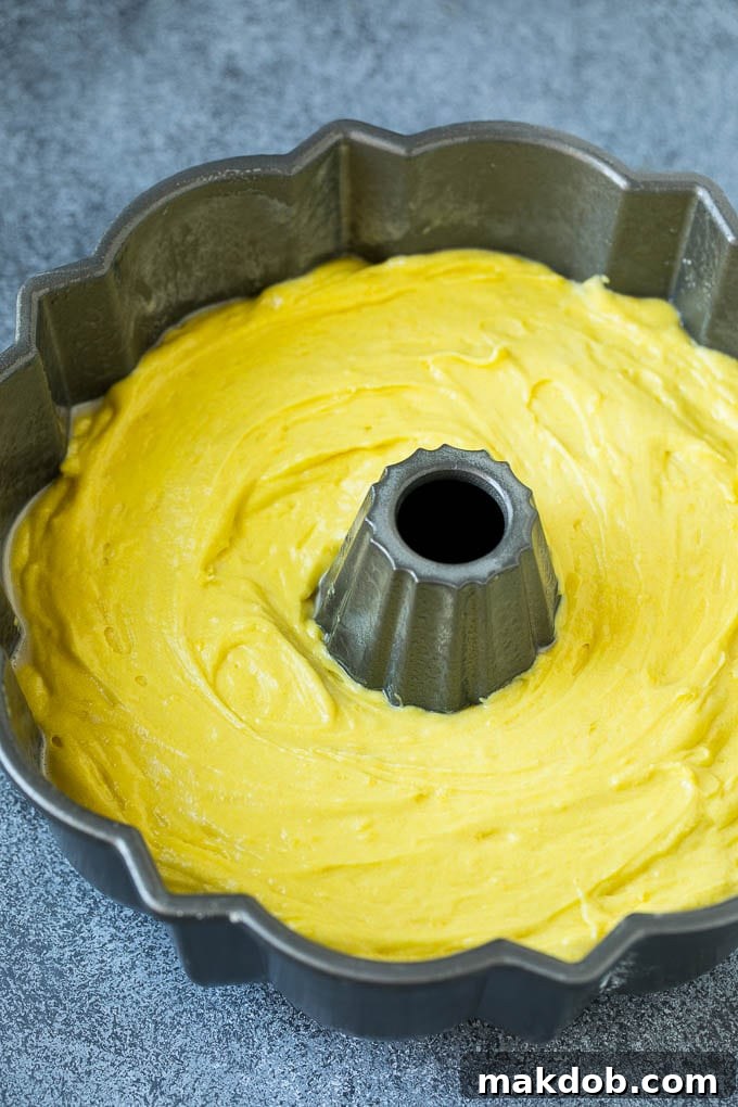 Lemon cake batter being poured into a greased and floured bundt pan, ready for baking.
