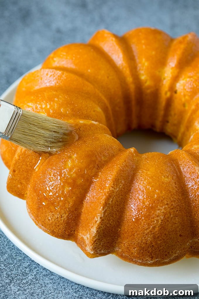 A pastry brush applying a glistening lemon syrup to a warm bundt cake, enhancing its flavor and moisture.