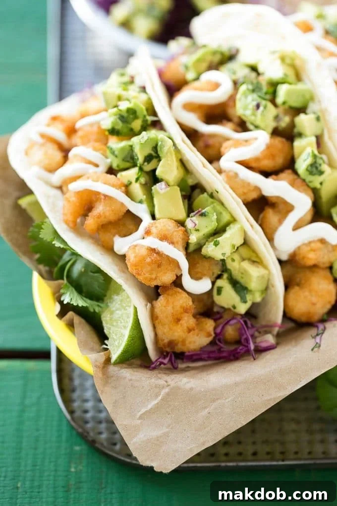Fried shrimp tacos in flour tortillas with avocado relish and sour cream, ready to eat.