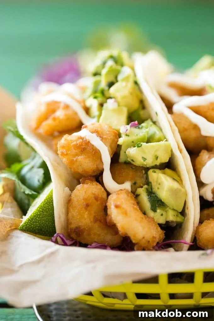 Fried shrimp tacos in flour tortillas with avocado and sour cream, close up view.