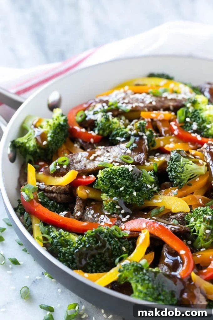 Close-up of beef teriyaki coated in homemade sauce, garnished with broccoli and vibrant sliced bell peppers.