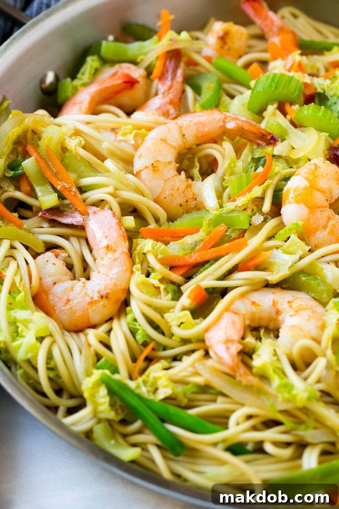 Close-up of succulent shrimp nestled amongst flavorful chow mein noodles and a medley of colorful, stir-fried vegetables in a pan.