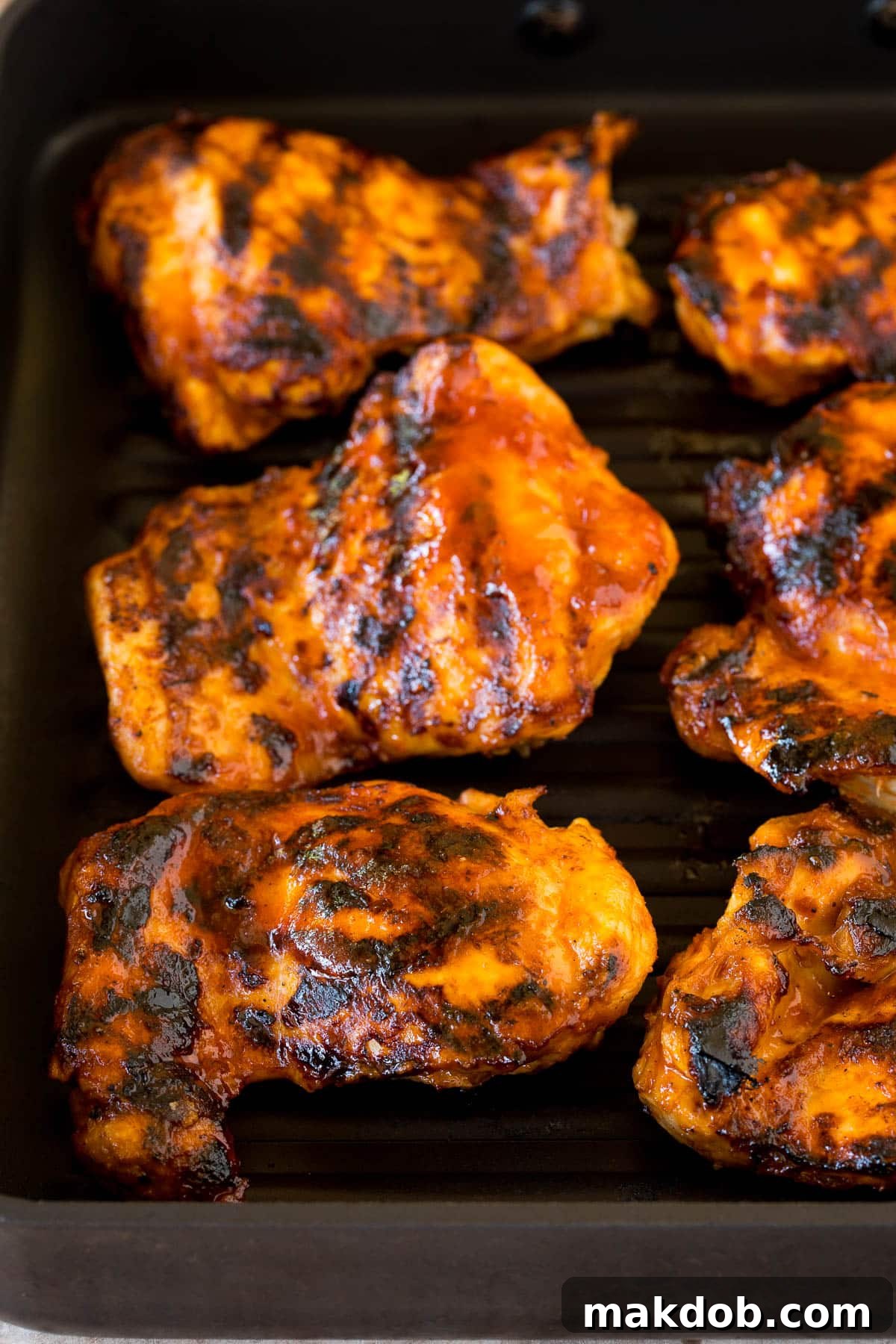 Expertly cooked chicken on a grill pan, showing delicious char marks and a glistening BBQ glaze.