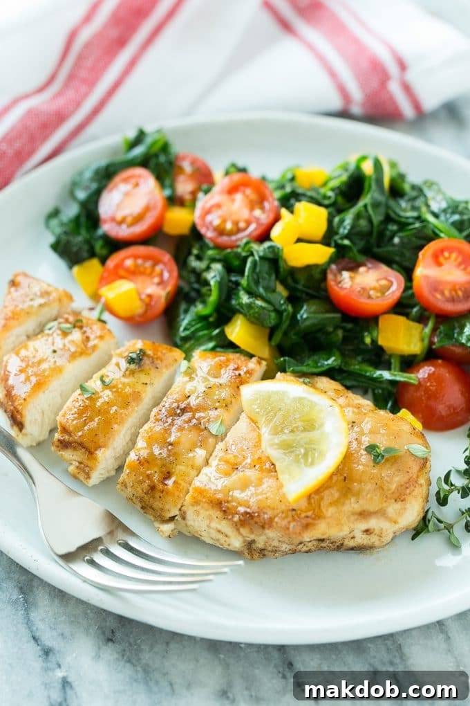 Golden-Brown Chicken & Wilted Spinach Skillet 5 A plate featuring perfectly sliced pan seared chicken breast, served alongside sautéed spinach and cherry tomatoes, drizzled with sauce.