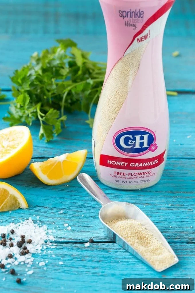 A close-up shot of key ingredients for lemon thyme chicken: honey granules, salt, pepper, fresh parsley, and lemon wedges.