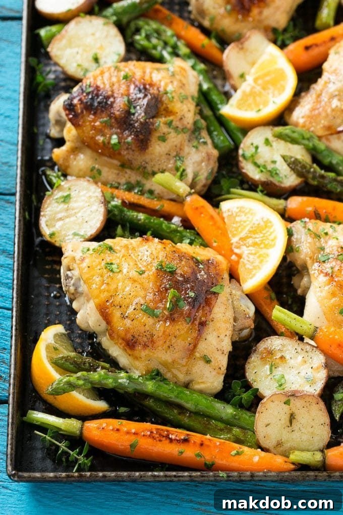 A sheet pan loaded with seasoned lemon thyme chicken thighs, new potatoes, carrots, and asparagus, ready for roasting.
