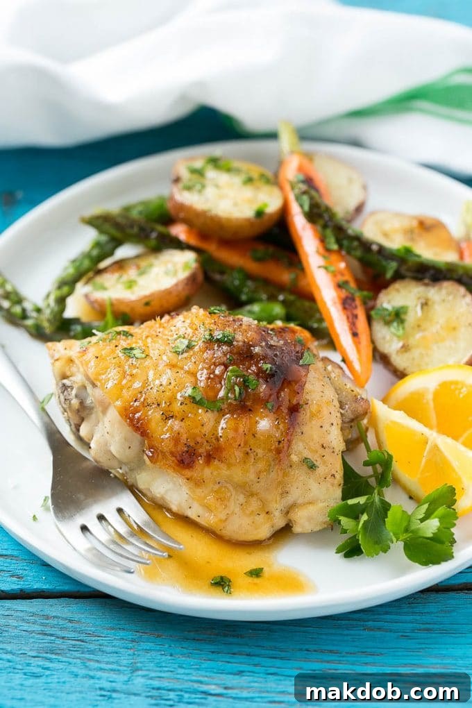 A plated serving of lemon thyme chicken, accompanied by perfectly roasted vegetables and new potatoes, garnished with fresh herbs.