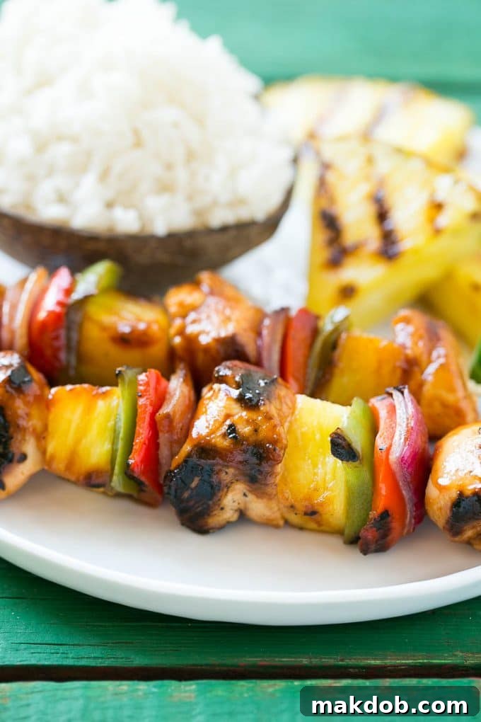 A beautifully plated serving of Hawaiian chicken kabobs, artfully arranged next to a mound of fragrant coconut rice and garnished with fresh green herbs.