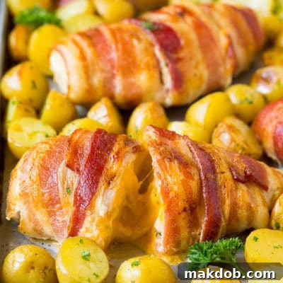 Bacon wrapped stuffed chicken breast on a sheet pan with roasted potatoes.