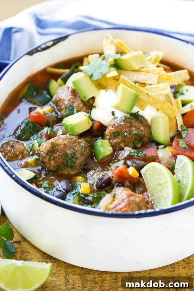 A pot of meatball soup with corn, beans and carrots, topped with sour cream and avocado.