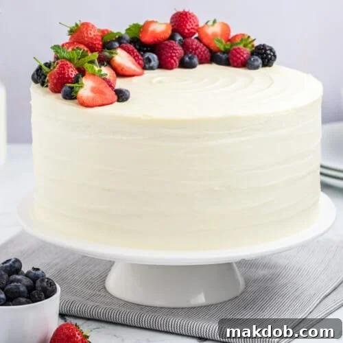 A berry chantilly cake on a cake stand, topped with fresh berries and mint sprigs.