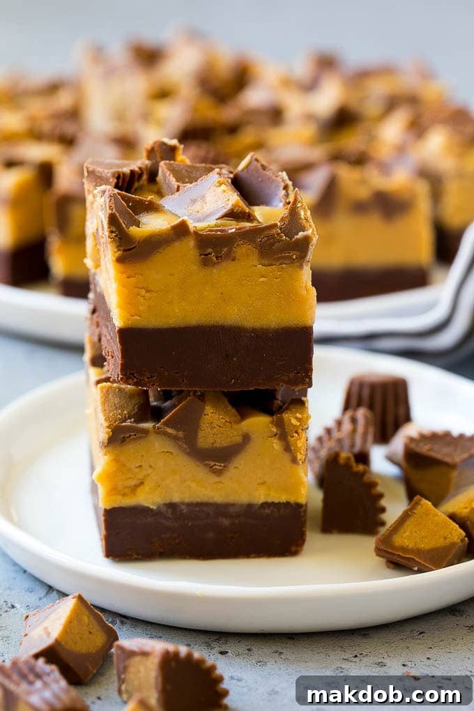 Easy Layered Chocolate Peanut Butter Fudge Recipe with Peanut Butter Cups Stacked pieces of rich chocolate peanut butter fudge topped with mini peanut butter cups on a white plate, showcasing the distinct layers.