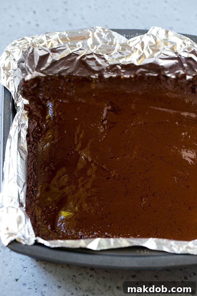 First Layer: Decadent Chocolate Fudge Base A perfectly smooth layer of chocolate fudge filling the bottom of a square baking pan, ready for the peanut butter layer.