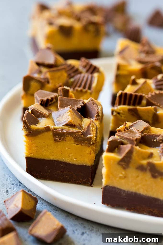 Serving-Ready Chocolate Peanut Butter Fudge Squares Perfectly cut squares of rich chocolate peanut butter fudge, each topped with a mini peanut butter cup, arranged invitingly on a white surface.