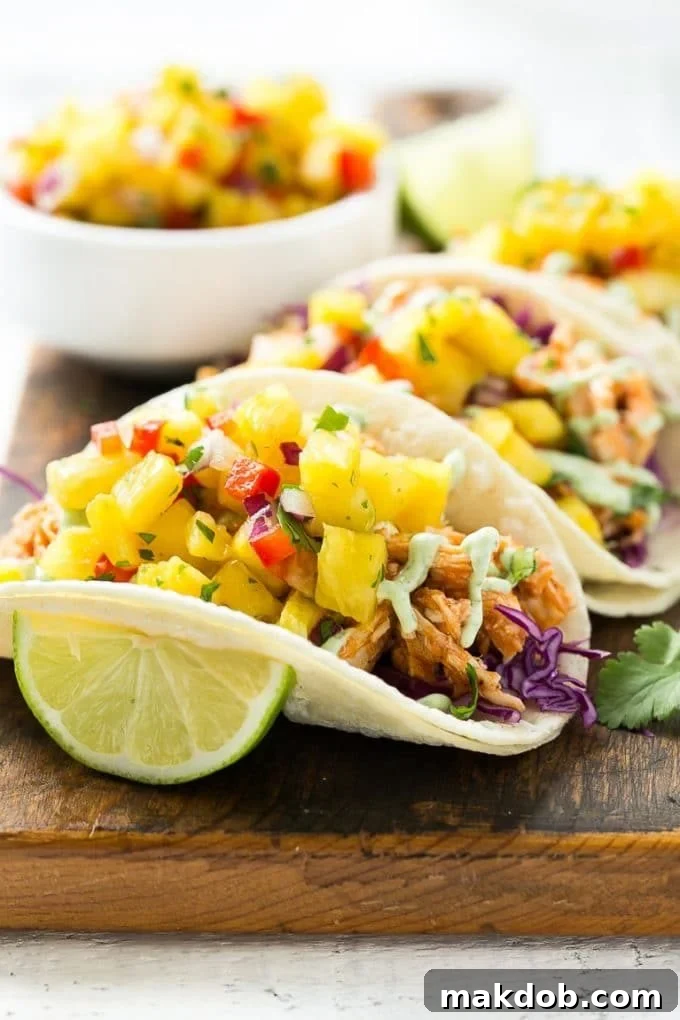 A vibrant platter of perfectly assembled pulled chicken tacos, generously topped with a colorful pineapple salsa and drizzled with creamy cilantro sauce, ready to be enjoyed.