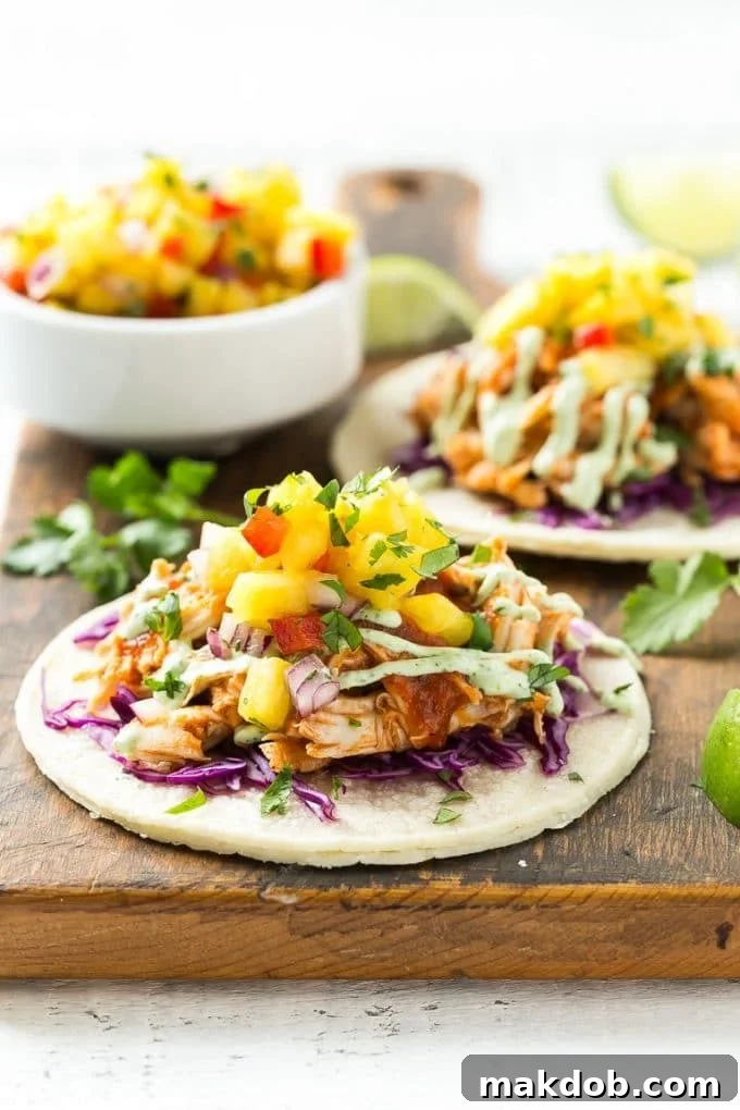A single mini corn tortilla generously filled with tender pulled chicken, crisp purple cabbage, and a vibrant pineapple salsa, ready to be folded.