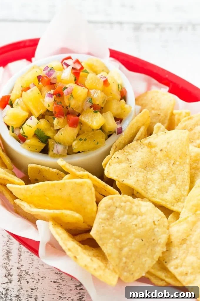 A vibrant bowl of homemade pineapple salsa, accompanied by crispy tortilla chips, perfect for a refreshing snack or taco topping.