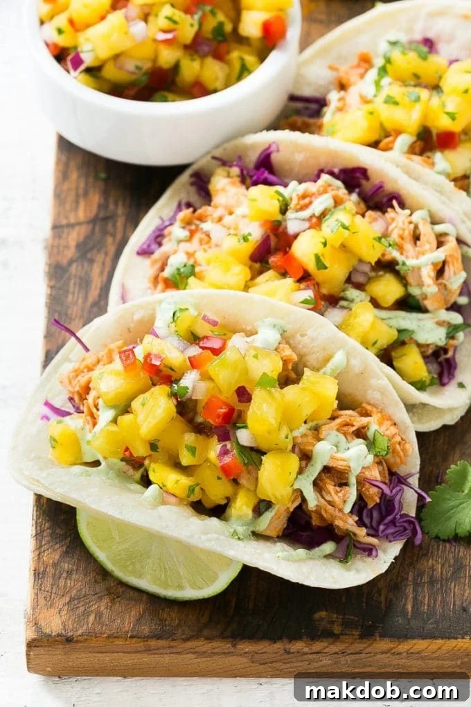 A close-up shot of a single pulled chicken taco, showcasing its colorful layers of shredded chicken, pineapple salsa, and cilantro sauce, tucked into a warm corn tortilla.