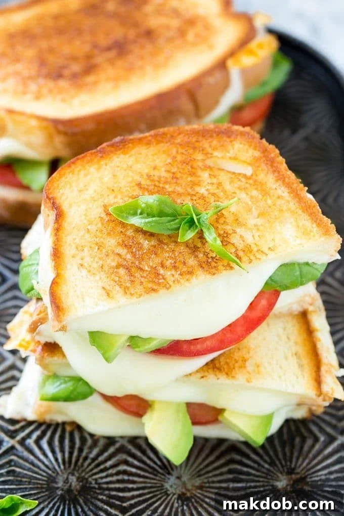 Close-up of a warm, grilled Caprese sandwich, revealing gooey melted cheese, vibrant red tomato slices, and rich green avocado, ready to be enjoyed.