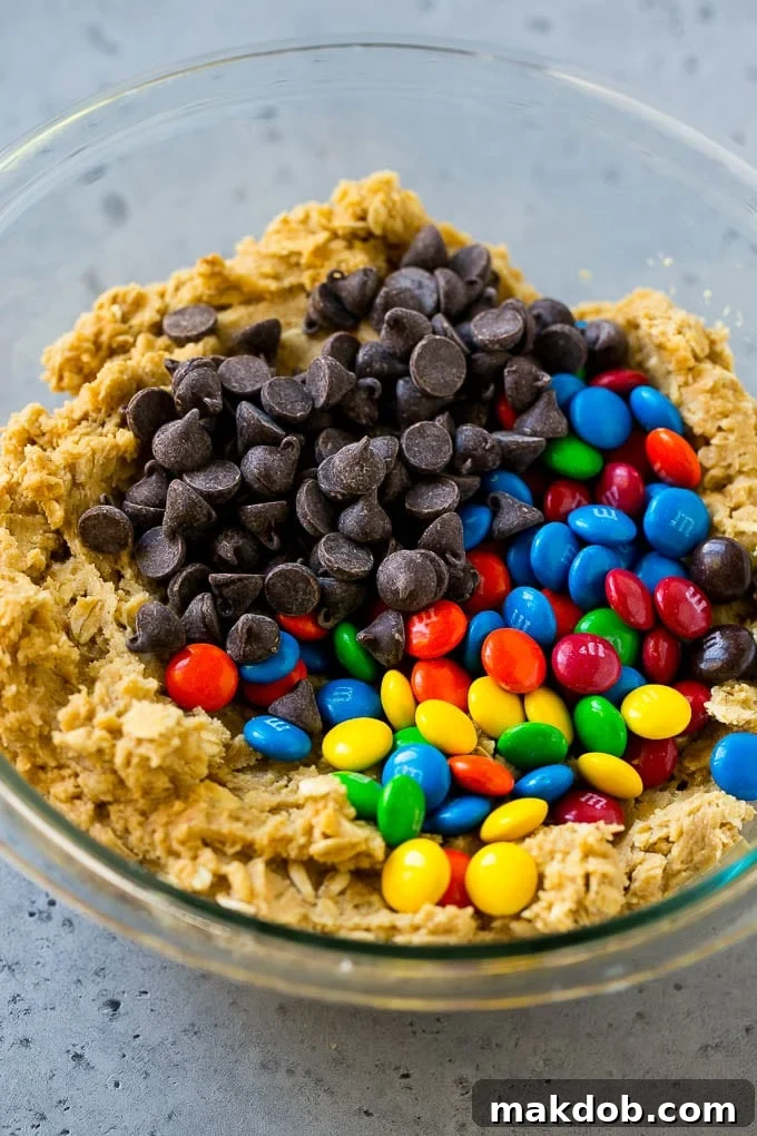 Perfectly Portioned Cookie Dough Ready for Baking Unbaked cookie dough balls, generously topped with chocolate chips and M&M's, ready for baking on a parchment-lined sheet.