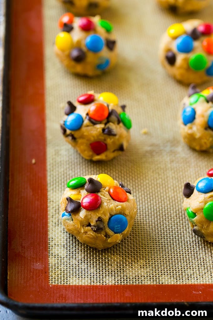 Pre-baked Monster Cookie Dough on Baking Tray Balls of freshly scooped Monster Cookie dough, adorned with colorful M&M's and chocolate chips, perfectly spaced on a baking sheet awaiting the oven.
