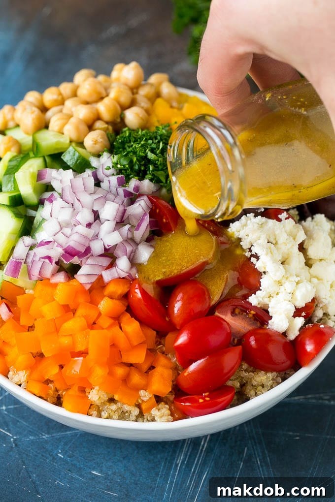 Dressing being poured over a bowl of vegetables and quinoa.