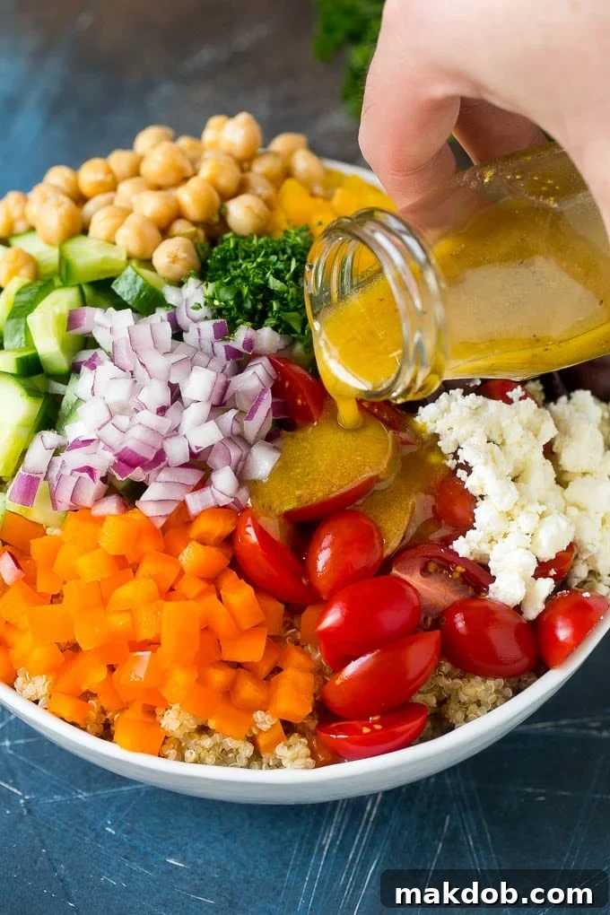 Dressing being poured over a bowl of vegetables and quinoa.