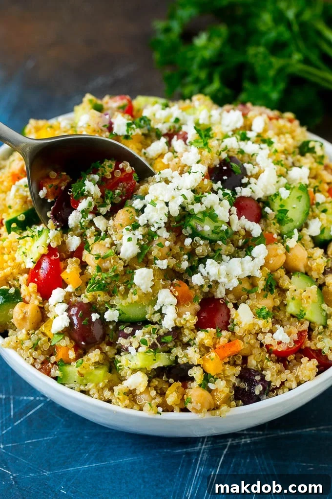 A serving spoon in a bowl of quinoa salad with feta and vegetables.