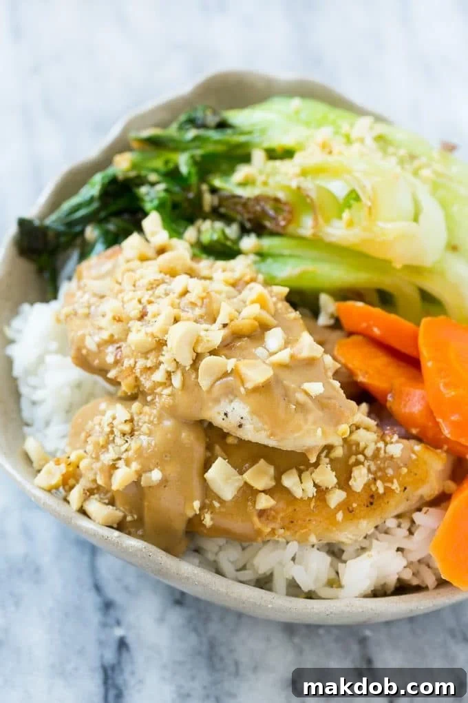 Thai Peanut Chicken Bowl with Steamed Rice A tantalizing bowl of Thai peanut chicken and colorful vegetables, served generously over a bed of steamed rice, highlighting a complete and appetizing meal.