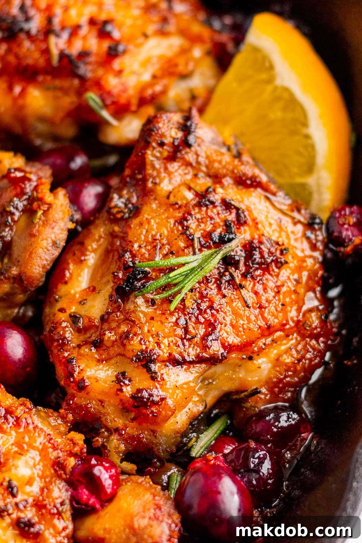 Cranberry chicken in a skillet garnished with orange slices and fresh rosemary.