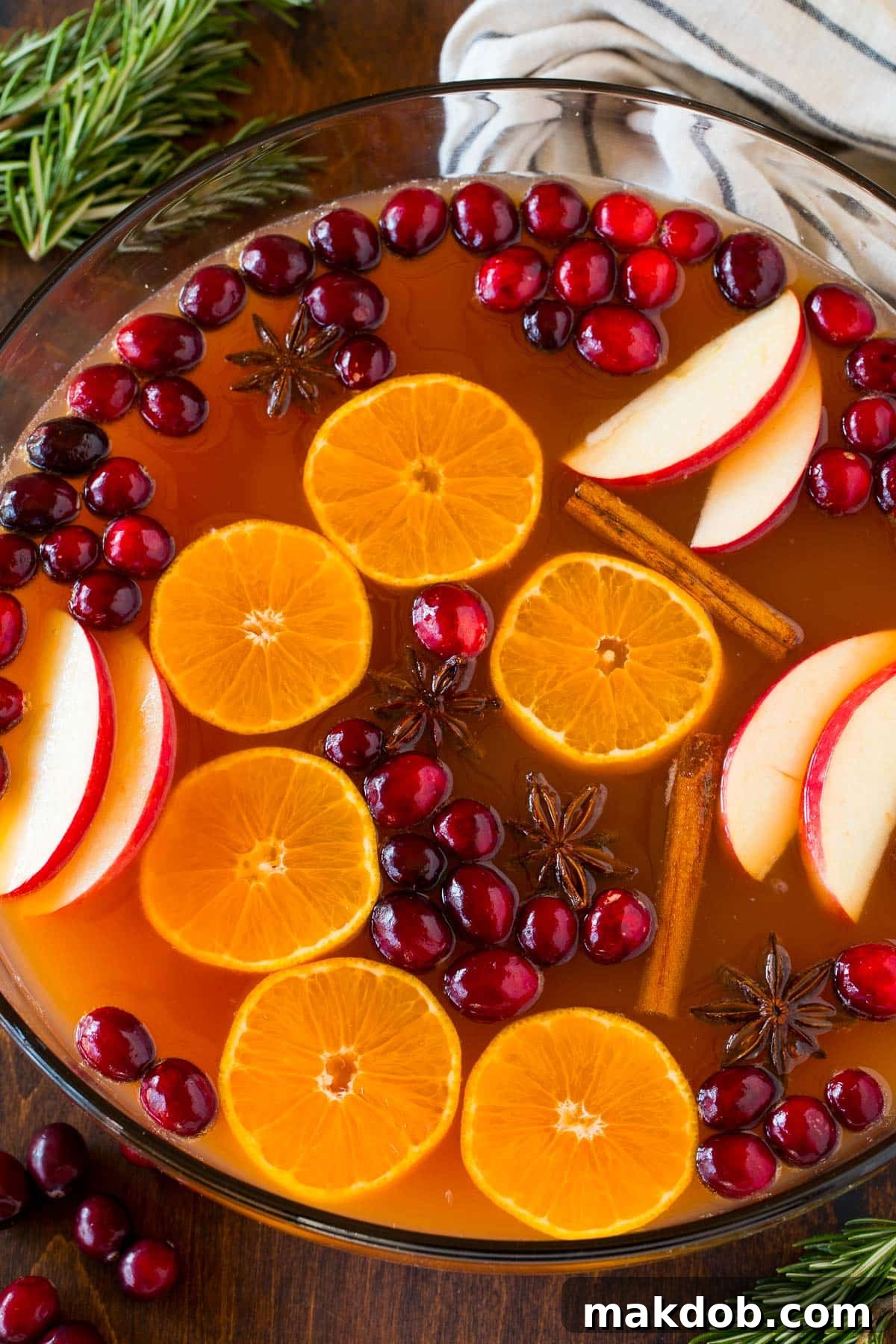 Thanksgiving punch in a large glass punch bowl, beautifully garnished with floating apple slices, orange wheels, and fresh cranberries.