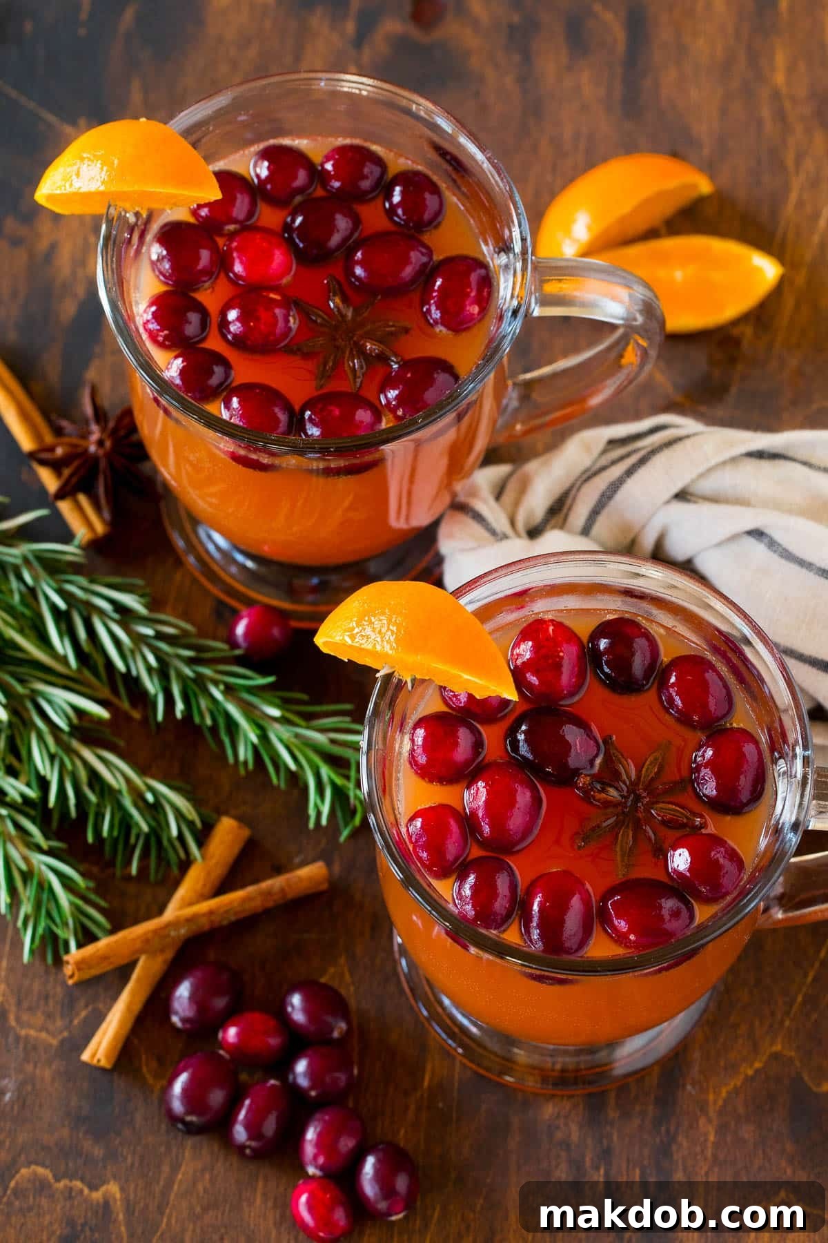 Two festive glasses filled with Thanksgiving punch, garnished with cinnamon sticks, orange slices, and cranberries.