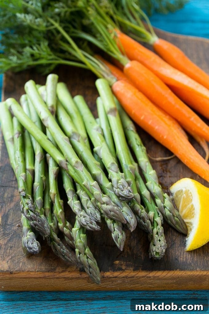 Chicken Primavera Recipe | Chicken Pasta | Vegetable Pasta #chicken #pasta #asparagus #carrots #peas #spring #dinner #dinneratthezoo Fresh asparagus and baby carrots on a wooden cutting board, prepped for cooking.