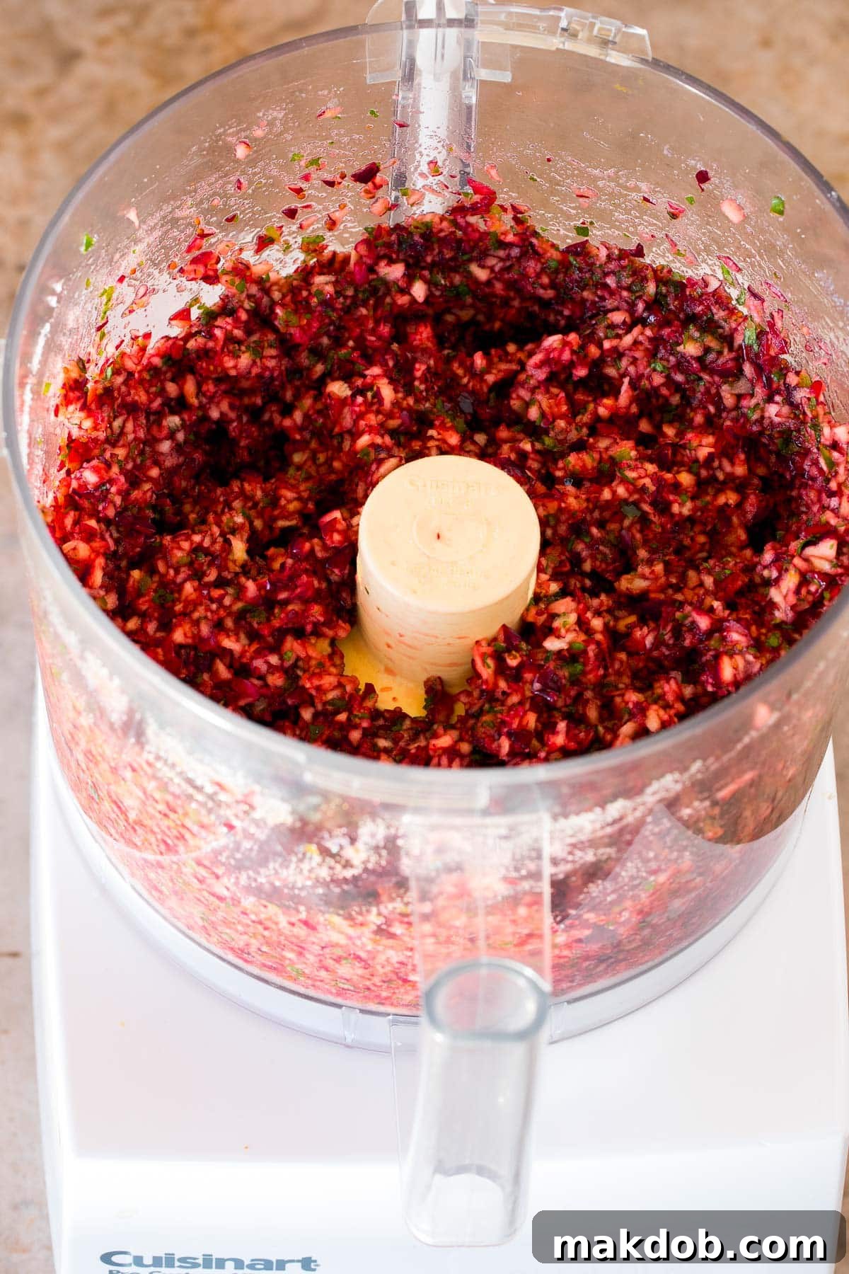 Close-up shot of vibrant cranberries, fresh herbs, and sugar finely ground and blended together in a food processor, showcasing the perfect salsa texture.