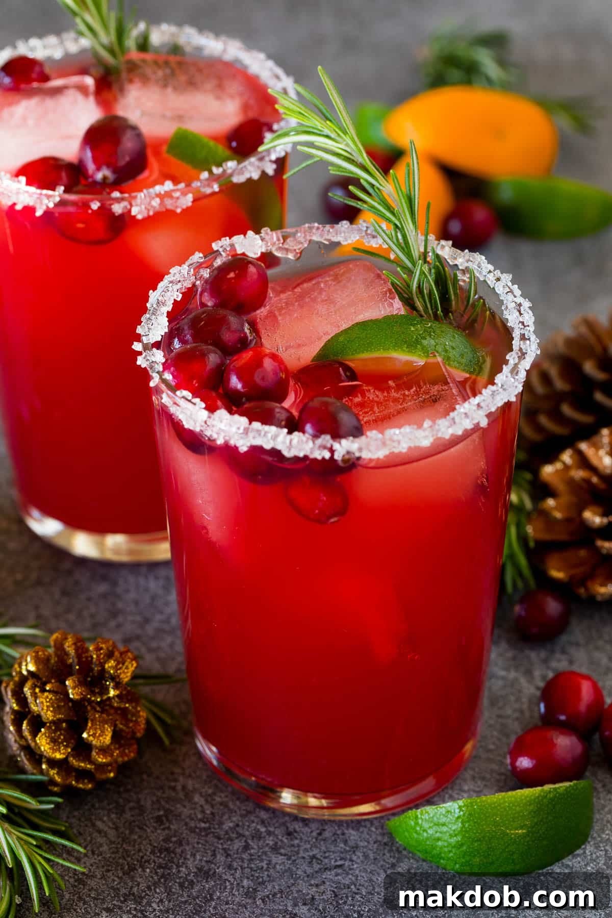 Jingle Bell Margarita 2 A beautiful Christmas margarita with a sugar and salt rim, garnished with fresh cranberries, a lime wedge, and a sprig of rosemary, set against a festive backdrop.