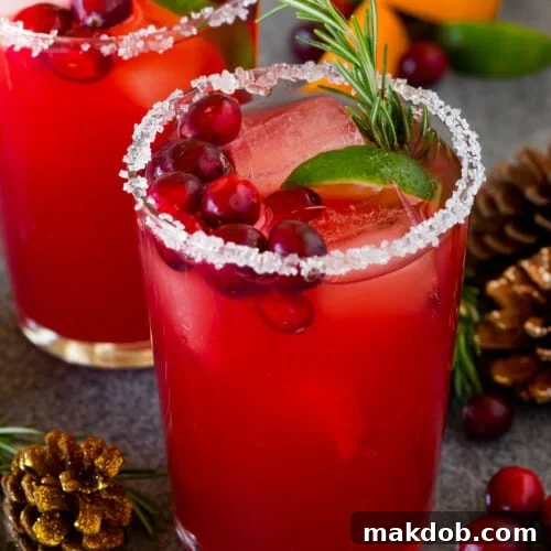 A Christmas margarita with a sugar rim on the class, and garnishes of cranberry, lime and rosemary.