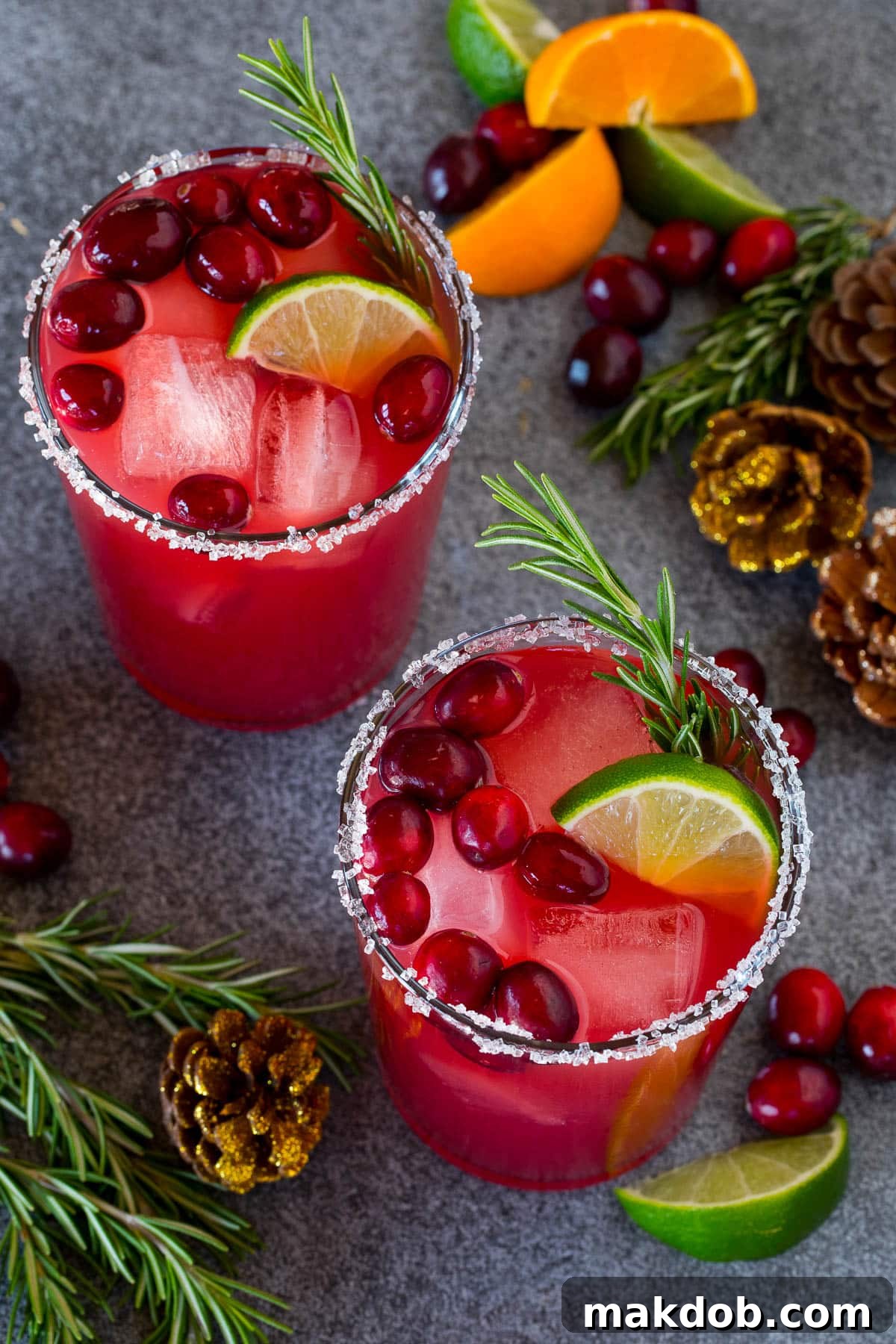 Jingle Bell Margarita 6 Two beautifully presented Christmas margaritas, each with a sugar and salt rim, adorned with fresh cranberries and a sprig of rosemary.