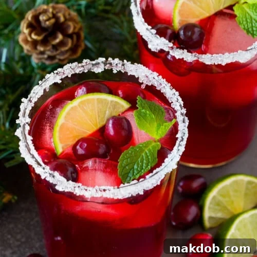A cranberry margarita in a sugar-rimmed glass with garnishes of fresh berries, lime, and mint.
