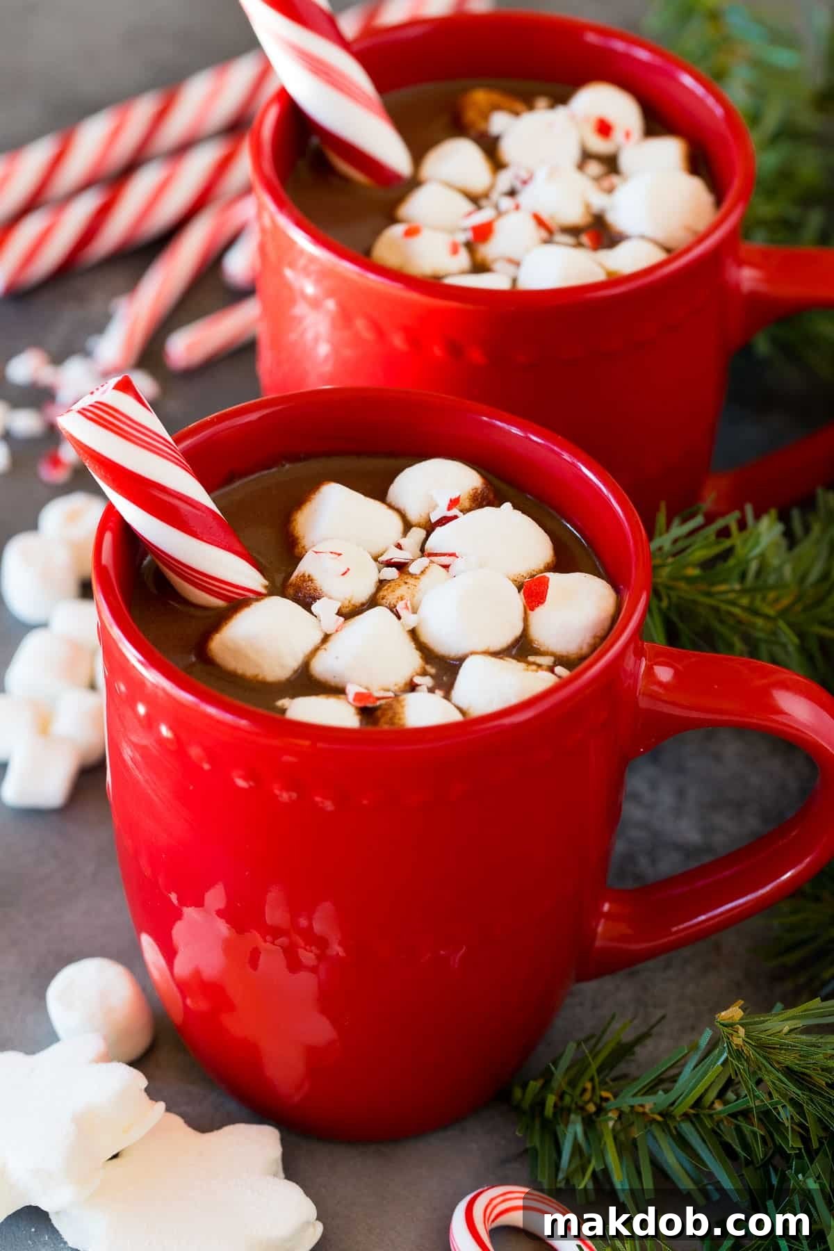 Peppermint Cocoa Bliss 2 Mugs of peppermint hot chocolate topped with marshmallows and a peppermint stick.