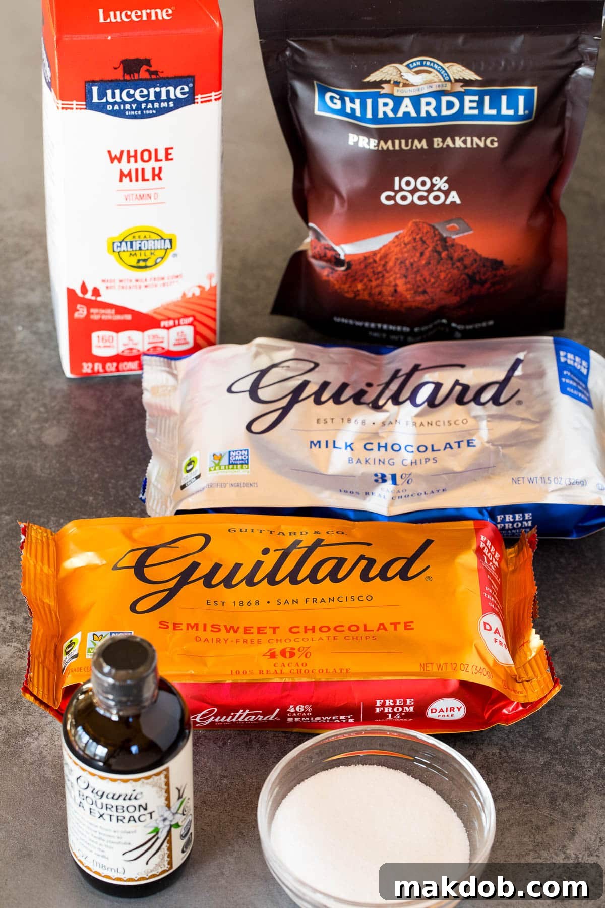 A beautiful flat lay of hot cocoa ingredients including fresh whole milk, various types of chocolate, unsweetened cocoa powder, and granulated sugar.