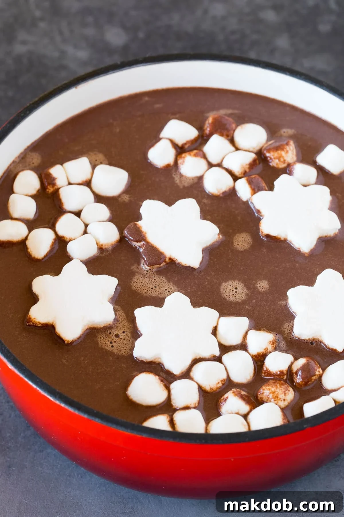 A pot of rich, dark hot chocolate adorned with an assortment of colorful marshmallows, ready to be served.