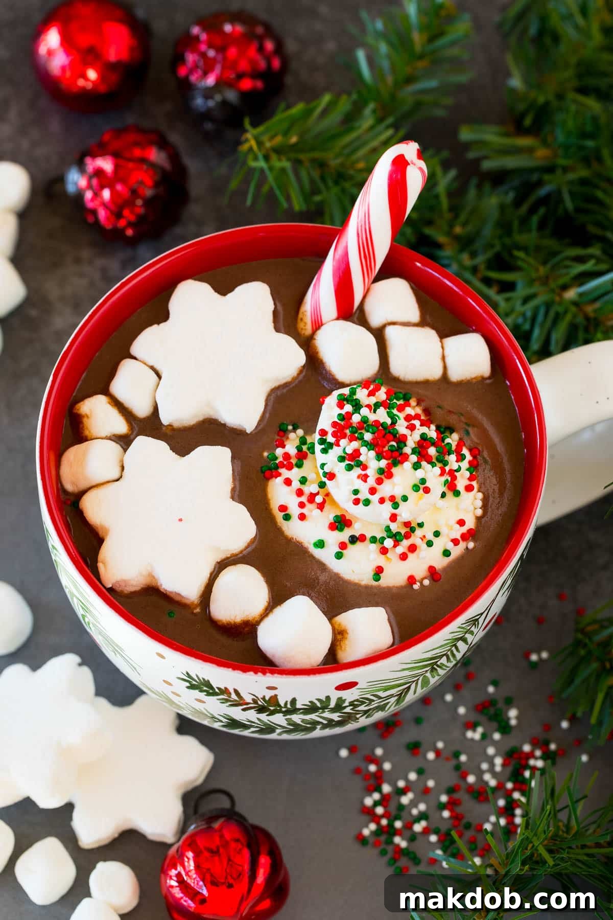 A beautifully garnished mug of Christmas hot chocolate with marshmallows and sprinkles, presented in a festive setting.